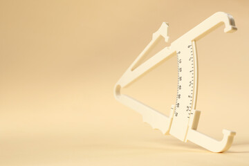 Plastic body fat caliper on beige background, closeup. Space for text