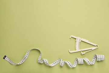 Body fat caliper and measuring tape on light green background, flat lay. Space for text