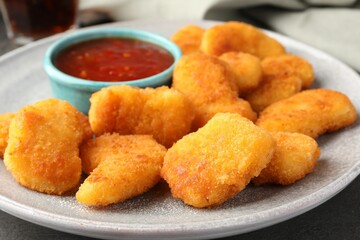 Plate with hot chili sauce and nuggets on grey table, closeup