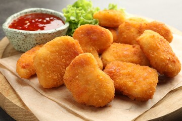 Board with hot chili sauce, lettuce and nuggets on table, closeup