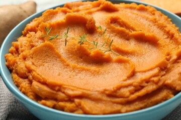 Tasty mashed sweet potato and thyme in bowl on table, closeup