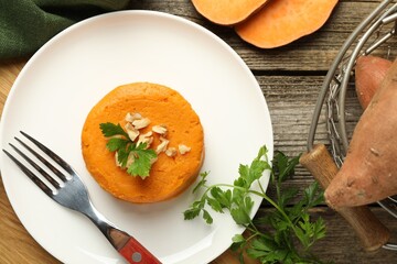 Tasty mashed sweet potato, parsley and walnuts served on wooden table, flat lay
