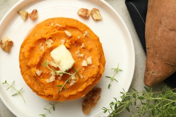 Tasty mashed sweet potato, butter, thyme and walnuts on grey table, flat lay