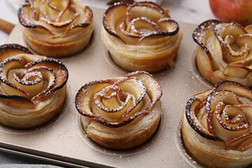Freshly baked apple roses in cupcake pan on table, closeup. Puff pastry