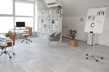 Interior of light open space office with workplaces, shelving unit and armchairs
