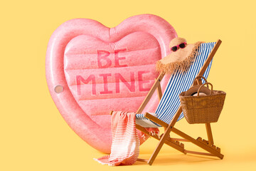 Inflatable mattress in shape of heart and deck chair with beach accessories on yellow background....
