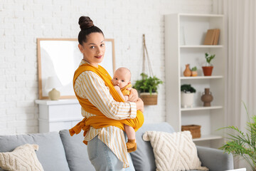 Beautiful young happy mother with cute little baby in sling at home