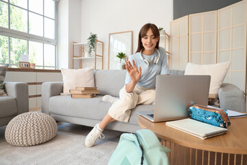 Happy female student with headphones, books and laptop video chatting at home