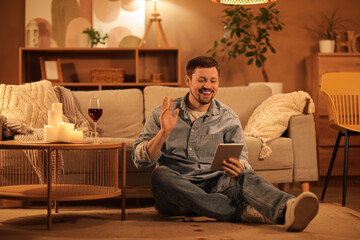 Handsome man with tablet computer having online date at home in evening