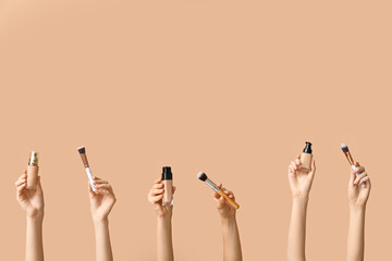 Female hands with bottles of makeup foundation and brushes on brown background