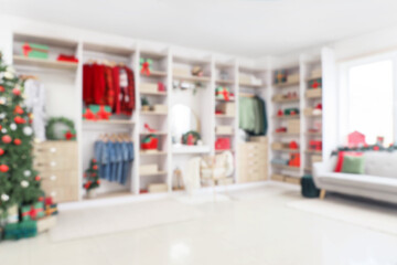 Modern wardrobe with stylish festive clothes, gift boxes and Christmas tree, blurred view