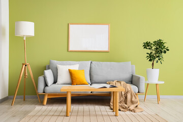 Interior of stylish room with grey sofa, pillows and coffee table near green wall