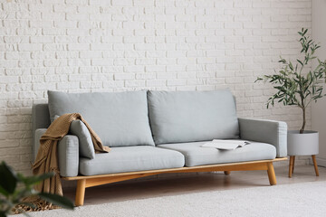 Stylish grey sofa with houseplant near white brick wall in room
