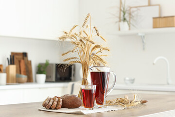 Jug and glass of tasty kvass with bread slices and spikelets on table in kitchen