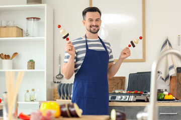 Young happy man cooking tasty fresh vegetables skewers near modern electric grill in kitchen