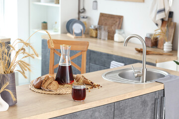 Jug and glass of tasty kvass with bread slices and spikelets on table in kitchen