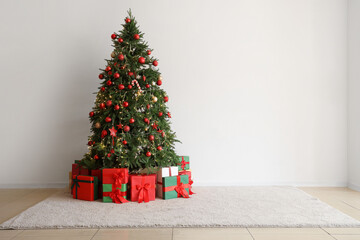 Christmas tree with presents near light wall in room