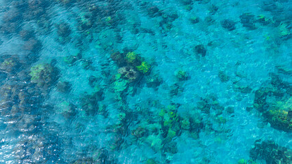Top view. Summer sea water, blue surface. The water is clear with ripples and sparkles in the sunlight and you can see coral under the sea