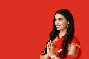 Naklejka premium Beautiful young happy Indian woman in traditional sari praying on red background. Divaly celebration