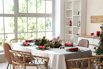 Dining table set for Christmas with burning candles and wreaths in room