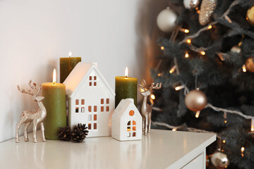 Burning candles with house shaped holders and Christmas decor on fireplace in room, closeup