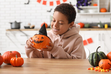Fototapeta premium Teenage African-American boy with Halloween pumpkin in kitchen