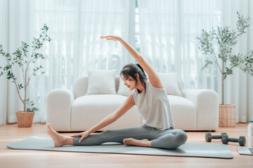 Happy young Asian woman practicing yoga and shoulder stretching at home sitting on floor in living...