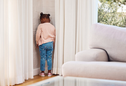 Home, back and kid in naughty corner for punishment in living room with behavior problem. Wall, attitude and girl child in timeout for discipline of attitude, tantrum or mistake in lounge at house.