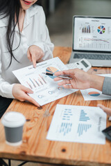 Close-up of business professionals discussing financial data and charts during a meeting, with a laptop and coffee cup on a wooden table.