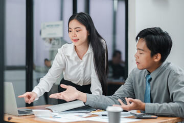Two young professionals engaged in a discussion while working on a laptop in a modern office environment.