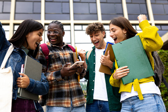 Cheerful students college friends receiving good news celebrating looking at phone together.