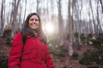 Portrait of pretty woman wearing a red jacket hiking in forest at sunset.