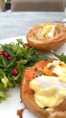 Eggs Benedict with salmon on croissant greens and pomegranate seeds served with coffee for complete breakfast. Crafted with eco-friendly ingredients, ideal for green lifestyle Fresh, satisfying.