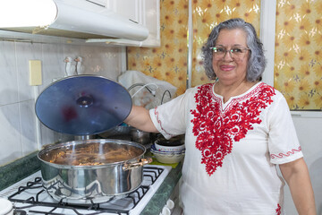 Mexican grandmother dressed in traditional costume from Puebla in front of casserole prepared the...