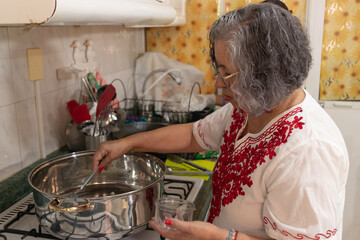 Mexican grandmother stewing the chopped onion in the ground beef stew to prepare the chiles en...