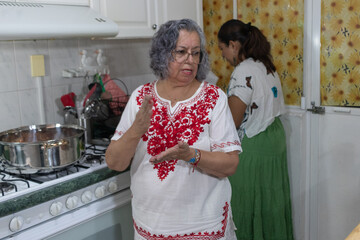 Women dressed in traditional Mexican clothing preparing to chop the ingredients needed to prepare...