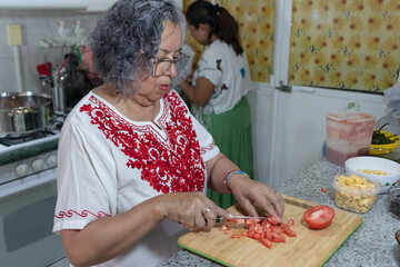 Mexican women chopping tomatoes on a chopping board and preparing poblano chiles along with the...