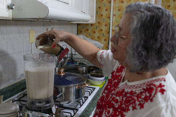 Mexican grandmother pouring milk into the blender to prepare the nogada sauce for the traditional...