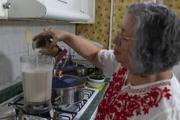 Mexican grandmother pouring milk into the blender to prepare the nogada sauce for the traditional...
