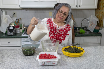 Mexican grandmother pouring freshly made nogada sauce into glass bowl to prepare traditional...