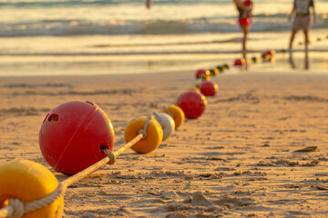 A line of colorful buoys resting on a sandy beach at sunset, gently curving towards the ocean, evoking a sense of calm and the rhythm of coastal life.Buoys create a safety zone for tourists