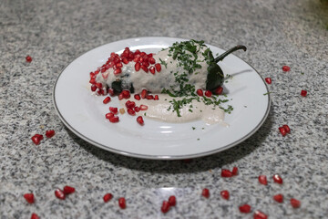 Traditional chile en nogada served on a white plate, the colors of the Mexican flag represented with parsley, nogada and pomegranate