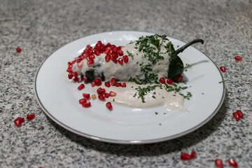 Traditional chile en nogada served on a white plate, the colors of the Mexican flag represented with parsley, nogada and pomegranate