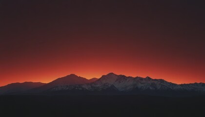 Obraz premium Silhouetted mountain range with snow-capped peaks against a fiery sunset sky.