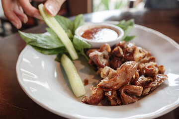 A plate of grilled pork intestines served alongside fresh basil, cucumber, and a spicy dipping sauce. 