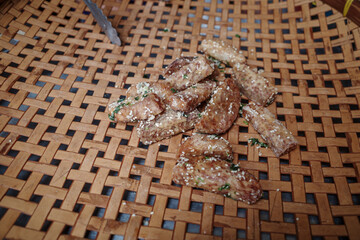 A close-up of crispy fried taro chips sprinkled with sesame seeds and herbs, arranged on a traditional woven bamboo tray. 