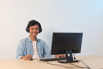 Portrait of excited Asian man playing video games on pc. Gamer enjoying his time in front of monitor. Isolated image on white background