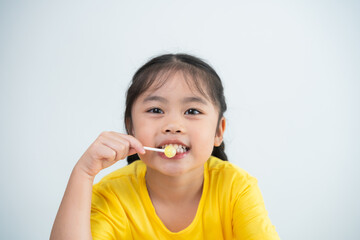 Asian young girl is smiling while holding a toothbrush. She is wearing a yellow shirt. Concept of innocence and playfulness