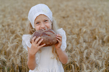Little beautiful blonde girl with rye bread in a field of ears of rye