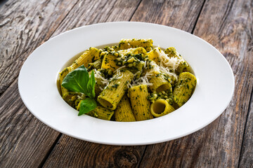 Pasta with basil pesto sauce and parmesan served in white bowl on wooden table
